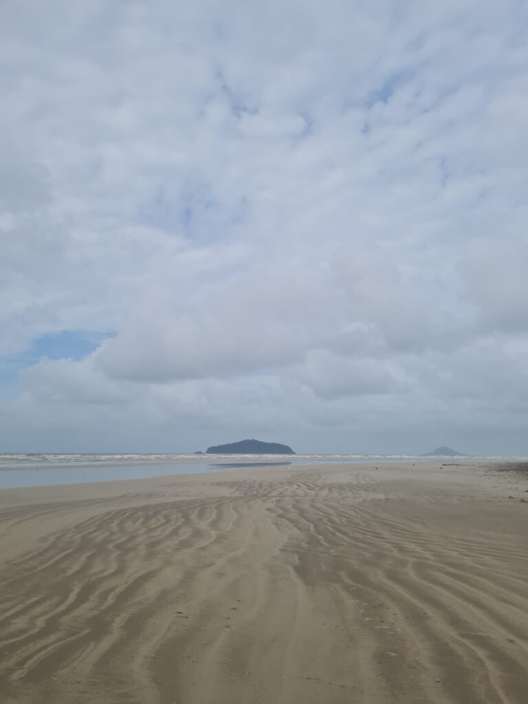 Sandy beach with track lines as though leading towards distant Sampadi island