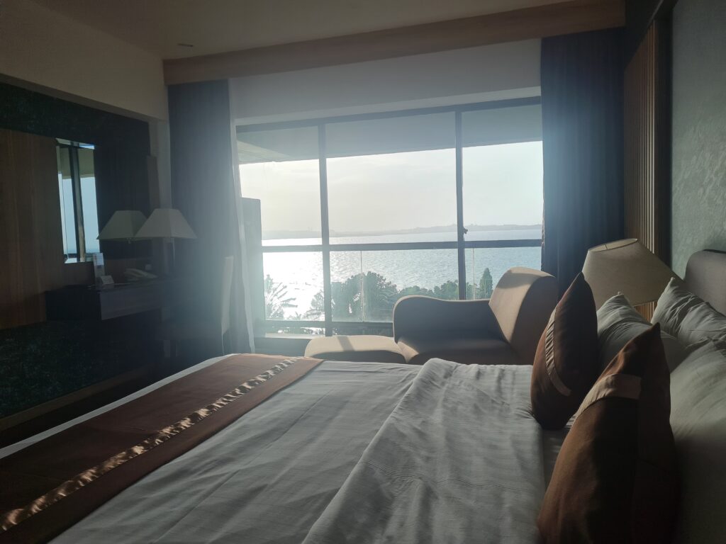 Hotel room interior at Batam View Beach Resort featuring a large bed and sea view window.