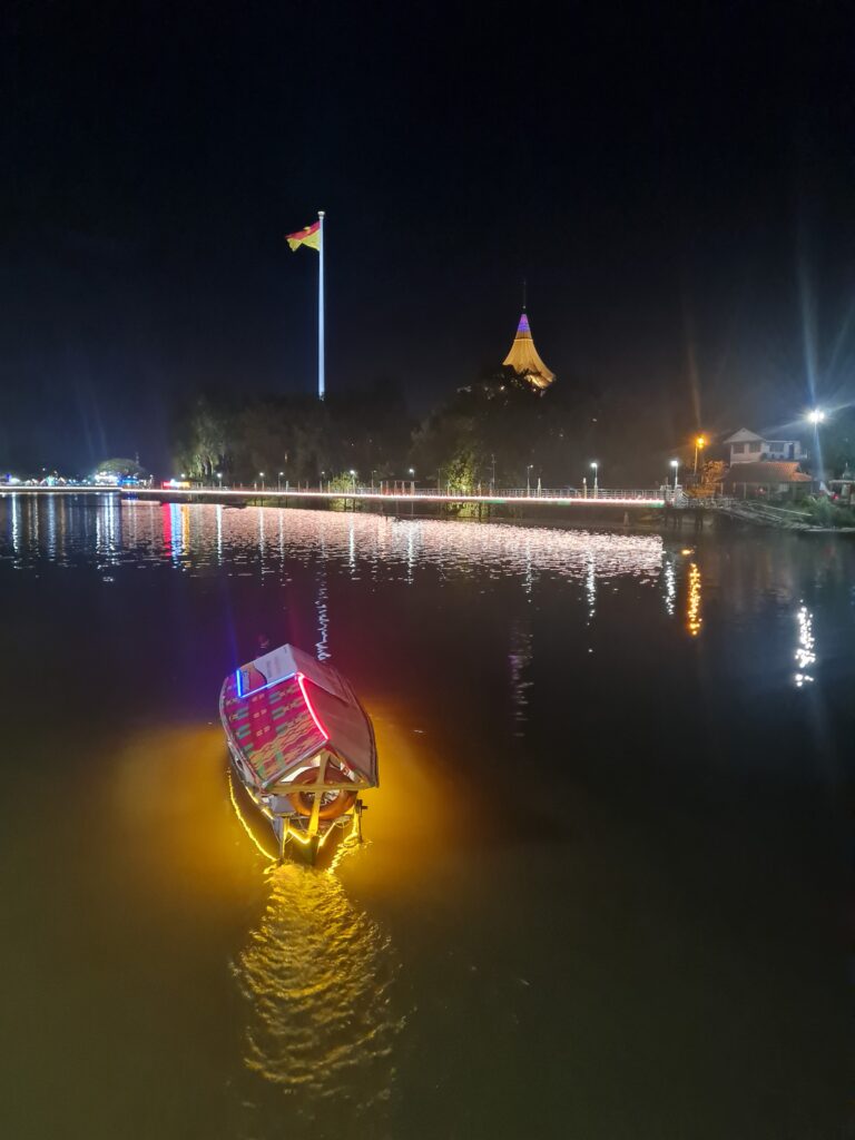 Night view of the Kuching Waterfront with a lit-up tambang boat and the DUN building in the background.