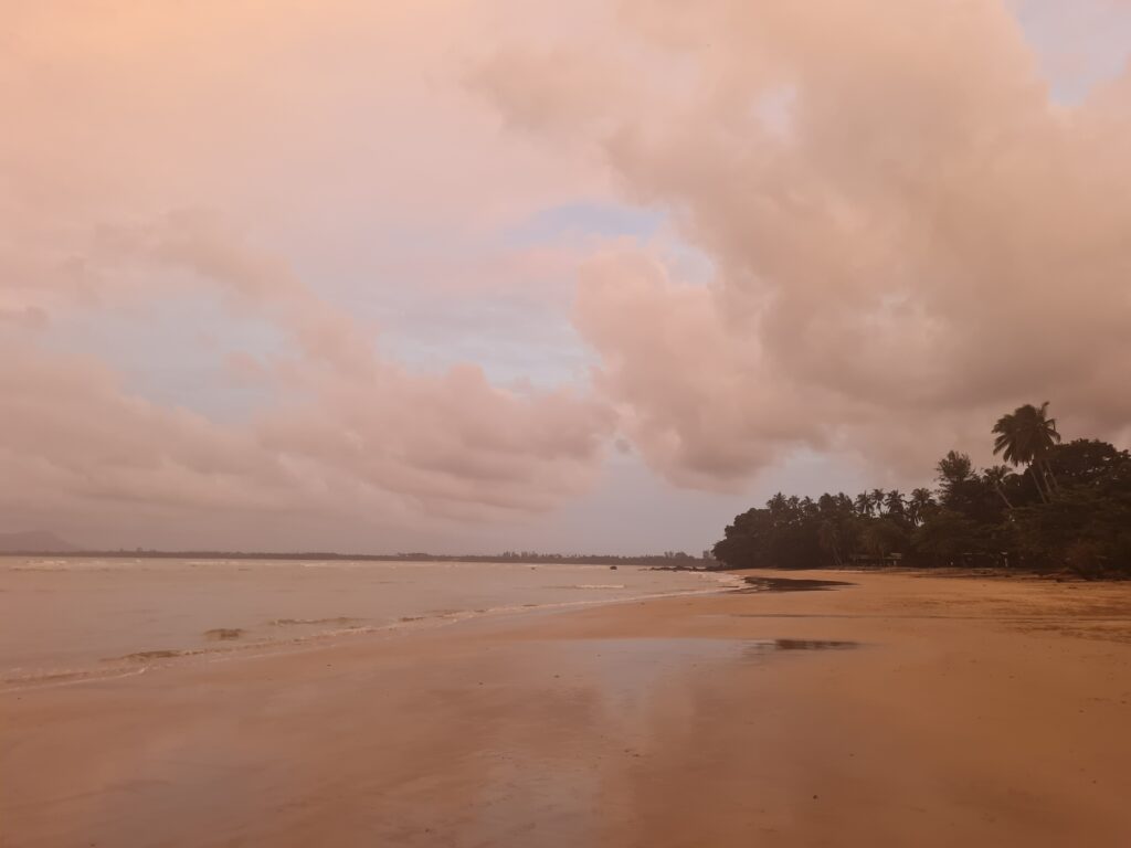 Wide angle view of the coastline at Siar Beach, Lundu, with soft pink sunset hues.