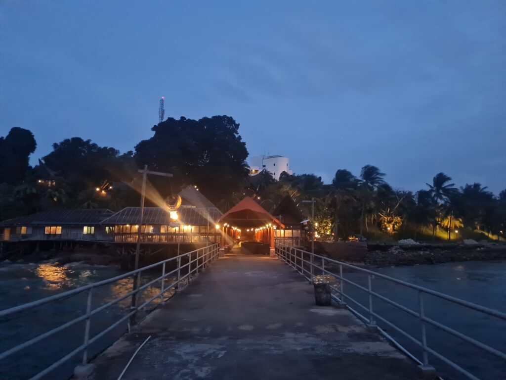 Long wooden pier walkway leading to the overwater restaurant, illuminated by warm lights.