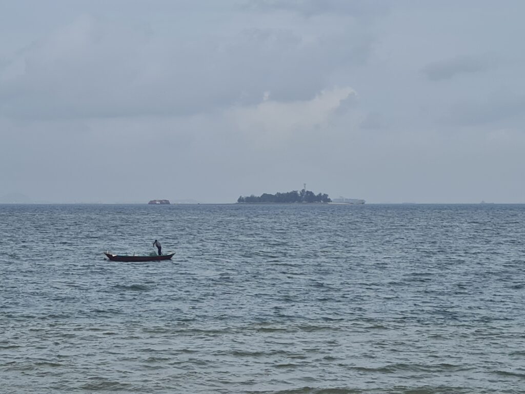 Lone fisherman in the middle ot the sea with a small island in the background.