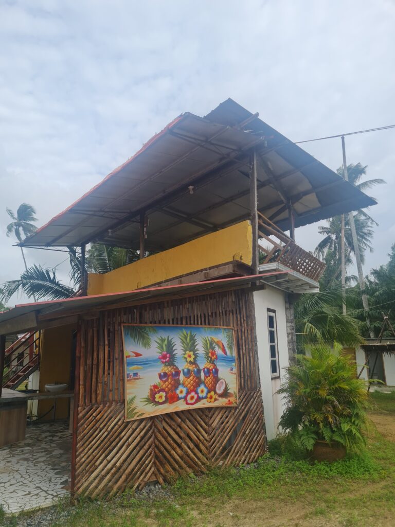 Bright yellow wooden chalet building at Redbee Camp Lundu with pineapple mural art.