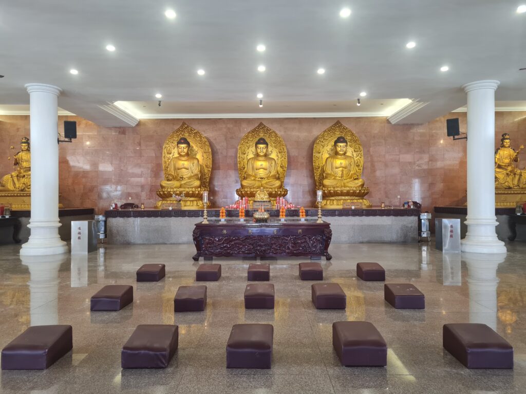 Interior view of the main hall at Duta Maitreya Monastery featuring three large golden Buddha statues.